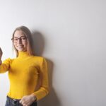 photo of woman in yellow turtleneck sweater blue denim jeans and glasses giving the thumbs up