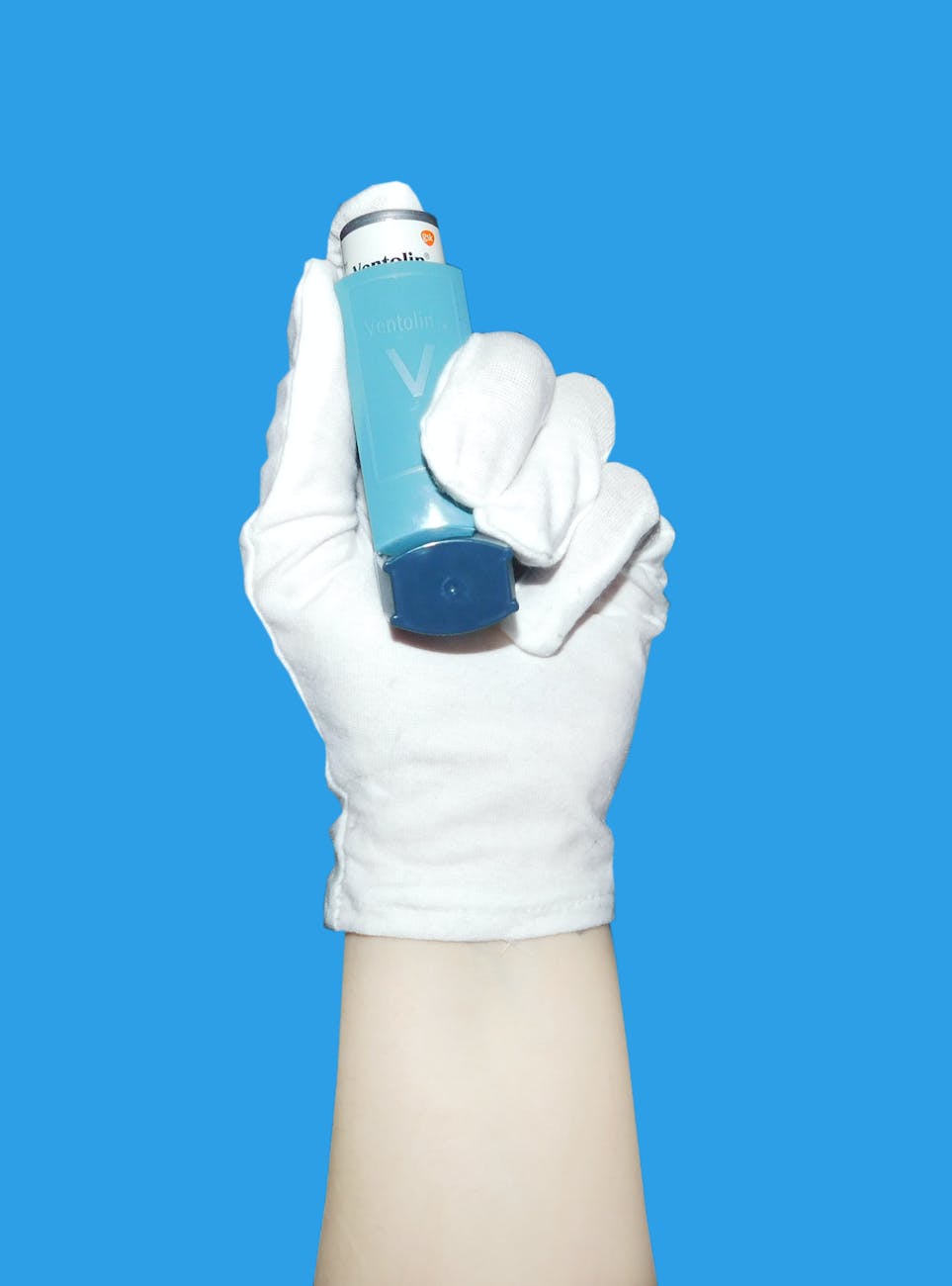 a hand wearing white gloves holding an inhaler